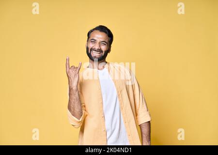 Felice uomo indiano che mostra rock n roll corna gesto mano isolato su giallo. Foto Stock