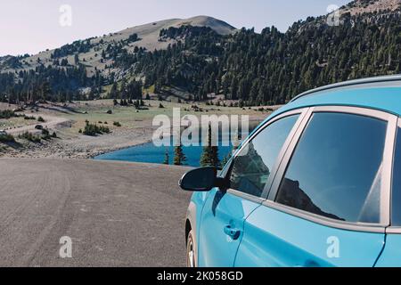 Auto blu sul lato della strada con vista sul lago di montagna. Viaggio estivo Foto Stock