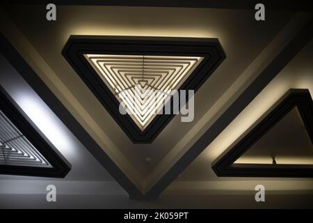 Sorgente luminosa triangolare. Luce nell'abitacolo. Luce di design. Dettagli dell'architettura. Soffitto nell'edificio. Foto Stock