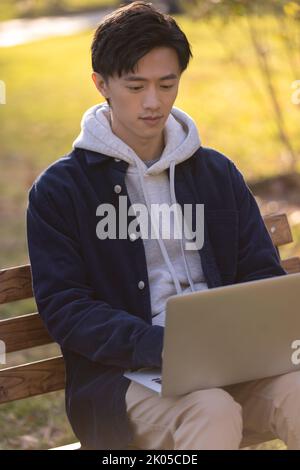 Felice studente universitario cinese che utilizza il computer portatile nel campus Foto Stock