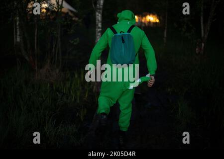 Uomo in vestito verde cammina attraverso i boschi. Ragazzo in costume divertente coccodrillo. Uomo a festival di musica in natura. Foto Stock