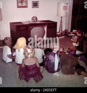 Vista posteriore dei bambini in costume che guardano una televisione alla festa di compleanno, ca. 1960. Foto Stock