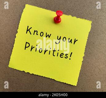 Conoscere il testo delle priorità su blocco note giallo con sfondo in legno. Concetto motivazionale. Foto Stock