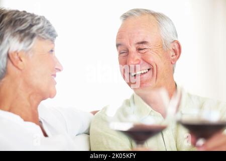 Tostatura in coppia con vino rosso. Uomo e donna sorridenti e maturi che brinda con vino rosso a casa. Foto Stock