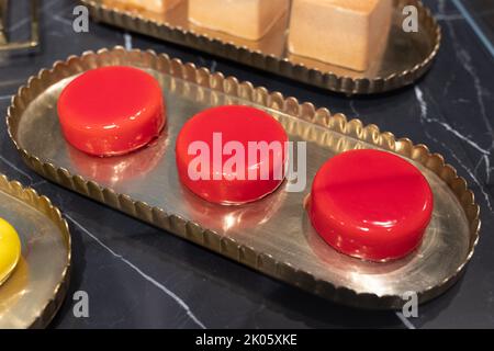 Tre piccole torte a forma rotonda e ricoperte di glassa rossa su un vassoio. Foto Stock