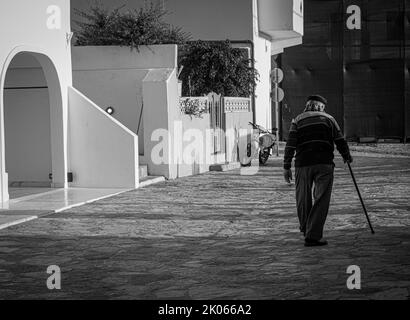 L'uomo anziano con canna cammina lungo la strada Foto Stock