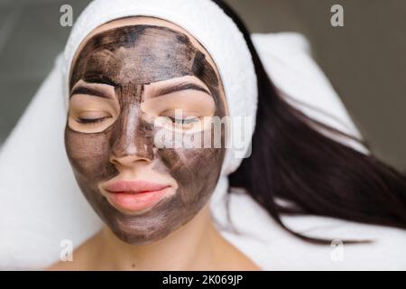 cosmetologo applicazione maschera nera sul viso bella donna indossare guanti neri, donna splendida in spa che hanno le procedure facciali Foto Stock