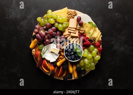 Tagliere di formaggi autunnali con frutta fresca e frutti di bosco serviti con vino bianco, vista dall'alto Foto Stock