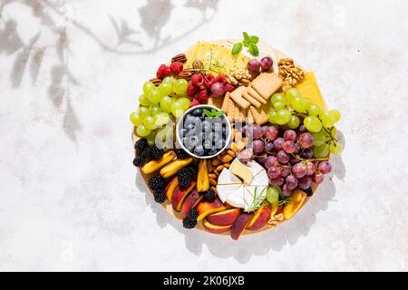 Tagliere di formaggi autunnali con frutta fresca e frutti di bosco serviti con vino bianco, vista dall'alto Foto Stock