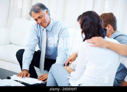 Giovane coppia che discute il piano finanziario con l'agente. Pianificatore finanziario maturo che spiega il programma finanziario con la coppia giovane nel paese. Foto Stock