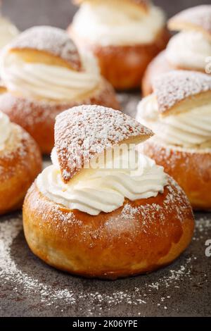 Semola dolce d'inverno tradizionale o fastlagsbulle aromatizzato con cardamomo, ripieno di pasta di mandorle e panna montata primo piano sul tavolo. Verticale Foto Stock