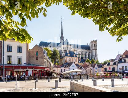 Cattedrale di Notre-Dame d'Amiens che si affaccia su Piazza Don, fiancheggiata da storiche case cittadine, caffè e ristoranti lungo il marciapiede in una giornata di sole estate. Foto Stock