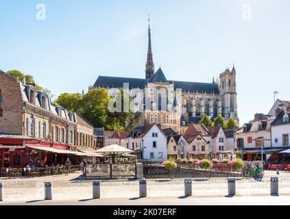 Cattedrale di Notre-Dame d'Amiens che si affaccia su Piazza Don, fiancheggiata da storiche case cittadine, caffè e ristoranti lungo il marciapiede in una giornata di sole estate. Foto Stock