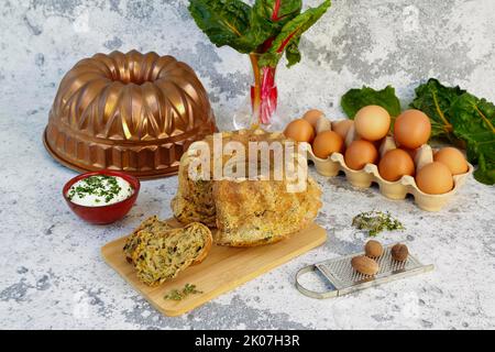 Cucina sveva, gugelhupf di bietole con salsa alle erbe, formaggio cagliato, pasticceria sostanziosa su tavola di legno, torta salata, vegetariana, cottura, cratere di noce moscata di fronte Foto Stock