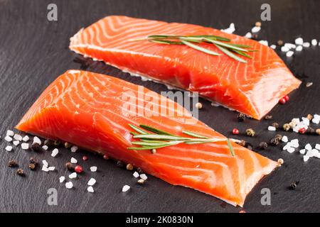 Due pezzi di filetto di salmone fresco con spezie su una superficie di ardesia nera Foto Stock