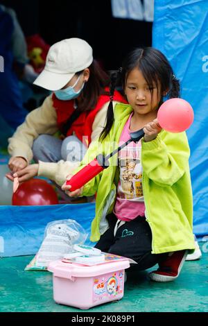 (220910) -- LUDING, 10 settembre 2022 (Xinhua) -- Un bambino dalla città di Detuo aiuta i volontari a saltare in aria palloncini al rifugio di sollievo del terremoto di Luding No. 2 High School in Luding, provincia sudoccidentale del Sichuan della Cina, 10 settembre 2022. Dopo un terremoto di magnitudo 6,8 che ha fatto scoppiare la contea di Luding nella provincia del Sichuan nel sud-ovest della Cina lunedì, più di 800 abitanti della città di Detuo, tra cui circa 50 bambini, sono stati temporaneamente delocalizzati nella scuola superiore di Luding n. 2. Dal settembre 6th, 11 insegnanti degli asili di Luding e 10 studenti universitari e superiori si sono offerti di prendersi cura di questi bambini. Foto Stock