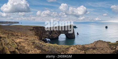 Pittoresca vista serale autunnale sulle scogliere della costa di Dyrholaey e sull'arco roccioso, Vik, Islanda del Sud. Reynisfjara oceano nero sabbia vulcanica spiaggia in lontano. Foto Stock