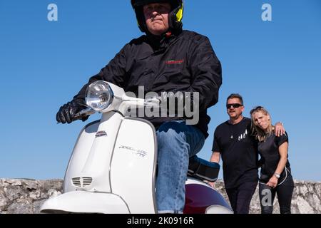 Uomo in sella a un classico scooter Lambretta bianco che lascia il rally di scooter al porto. Ballintoy, Regno Unito - 10 settembre 2022. Foto Stock