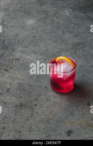 drink da cocktail con arbusto di mirtillo magenta rosa brillante con rotella al limone e ghiaccio su cemento Foto Stock