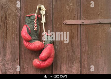 I vecchi guanti da boxe rossi in pelle appendono sullo sfondo del legno in marrone Foto Stock