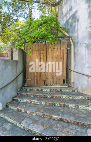 Scala esterna in pietra che conduce ad un cancello di legno di un edificio. La scala curva è contro la parete di un edificio con una vecchia porta d'ingresso in legno u Foto Stock