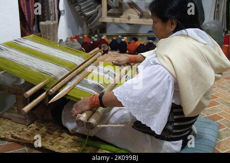 Tessitori al lavoro su telai a mano che fanno oggetti come tappeti o abbigliamento, nel mercato di Otavalo negli altopiani andini a nord di Quito Ecuador Foto Stock