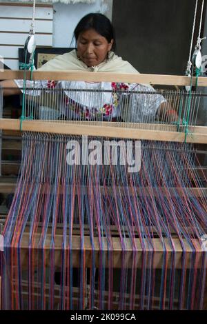 Tessitori al lavoro su telai a mano che fanno oggetti come tappeti o abbigliamento, nel mercato di Otavalo negli altopiani andini a nord di Quito Ecuador Foto Stock