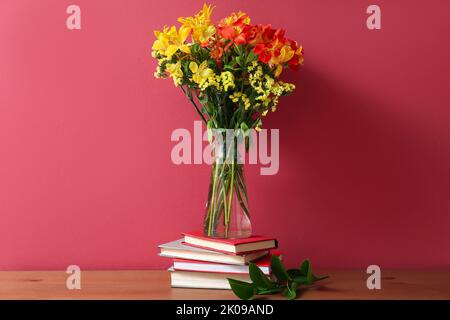 Pila di libri e vaso con fiori di alstroemeria sul tavolo vicino alla parete colorata Foto Stock