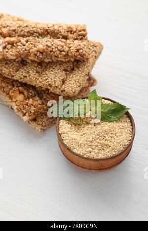 Saporite barrette kozinaki e ciotola di semi di sesamo su sfondo chiaro Foto Stock