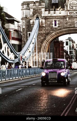 Un London Black Cab attraversa il ponte della torre in una soleggiata serata estiva nel centro di Londra. L'auto trasporta passeggeri in tutta Londra. Foto Stock