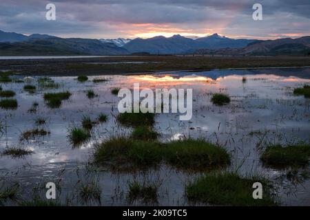 Sole che si trova dietro le montagne della valle di Jökulsá, nel punto in cui la circonvallazione (Route 1) attraversa il fiume Jökulsá í Lóni, Stafafell, Islanda Foto Stock