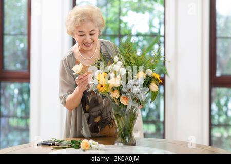 Donna cinese anziana felice che organizza i fiori a casa Foto Stock