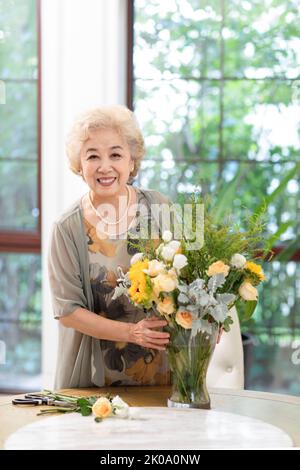 Donna cinese anziana felice che organizza i fiori a casa Foto Stock