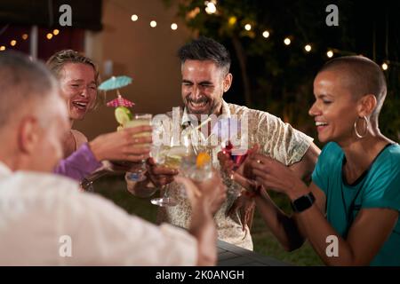 Gruppo di amici allegri a una festa serale brinda con cocktail e divertendosi insieme. Gente sorridente godendo la vita notturna bere alcolici Foto Stock