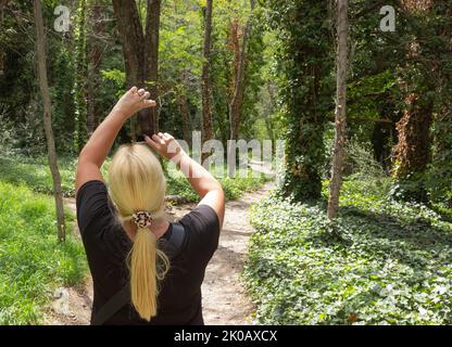 Donna bionda che fa una foto in una foresta. Foto Stock