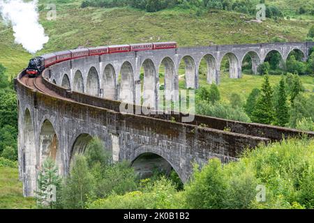 La locomotiva a vapore Jacobite e le carrozze ornate, attraversando l'iconico ponte viadotto, sulla West Highland Line, popolare località turistica e punto di riferimento, Foto Stock