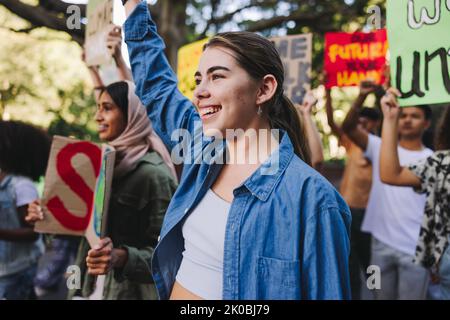 Giovani felici che si oppone al cambiamento climatico. Gruppo di attivisti giovanili multietnici che trasportano manifesti mentre marciano contro il riscaldamento globale. Di Foto Stock