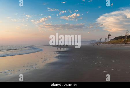 I visitatori della costa del Pacifico e le famiglie che camminano lungo la costa godendosi la tranquilla marea e il colorato tramonto al Beverly Beach state Park Foto Stock