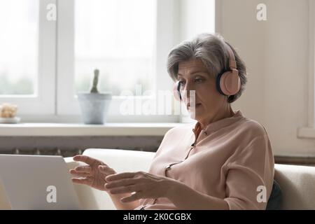 Donna blogger matura e focalizzata in cuffie wireless rosa con webinar Foto Stock