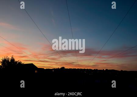 Cavi sopra un cielo tramonto con case residenziali Foto Stock