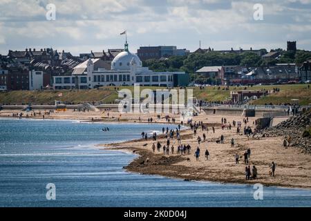 Spiaggia affollata in una giornata di sole a Whitley Bay, North Tyneside, Regno Unito, con la città spagnola sullo sfondo Foto Stock