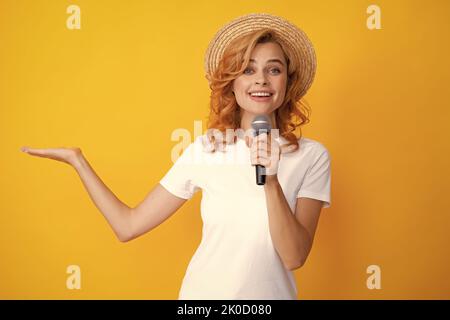 Elegante ragazza cantare canzoni con microfono, tenendo il microfono al karaoke, in posa su sfondo giallo. Foto Stock