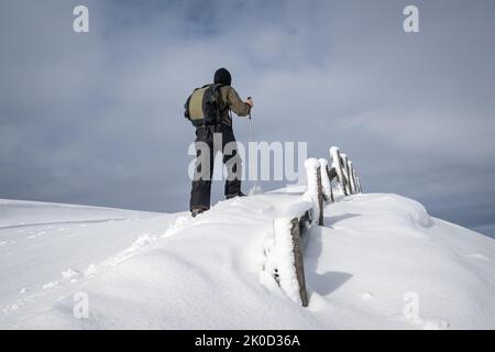 Un uomo che cammina sulla neve fresca, cielo moso sopra. Foto Stock