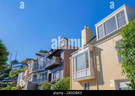 Fila di case suburbane vicino a un pendio con due torri sul retro a San Francisco, California. C'è una casa beige sul fronte con finestra allon baia Foto Stock