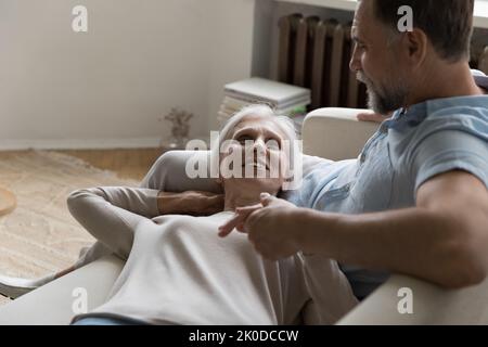Felice pacifica moglie matura sdraiata in divano, appoggiata al marito Foto Stock