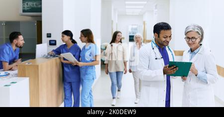 Giornata lavorativa in clinica medica, vista della hall con medici in cappotti bianchi, infermieri, assistenti e camminare lungo i pazienti corridoio dell'ospedale Foto Stock