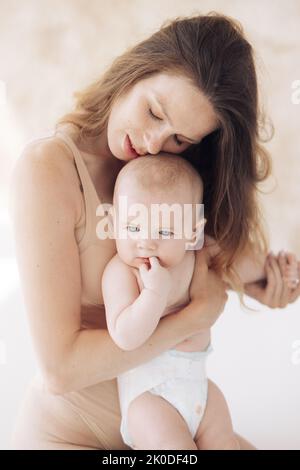 Giovane madre felice in bodysuit siede e abbraccia il suo bambino. Primo piano. Foto Stock