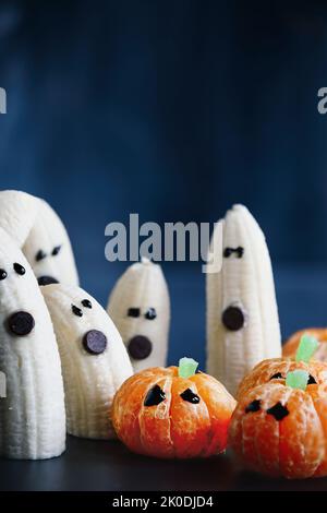 Halloween carino zucca arancia frutta e spaventoso banana fantasmi mostri con volti al cioccolato. Sano spuntino da dessert con volti divertenti per la festa dei bambini Foto Stock