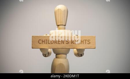 Uomo di legno che tiene in mano scritto diritti dei bambini segno su di esso. Questioni sociali. Foto Stock