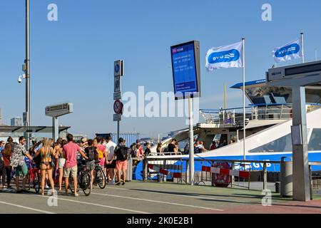 Amsterdam, Paesi Bassi - 2022 agosto: Folla di persone e ciclisti che catturano un traghetto fluviale dal centro della città Foto Stock